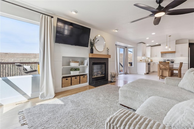 living room featuring a wealth of natural light, a ceiling fan, visible vents, and a tile fireplace
