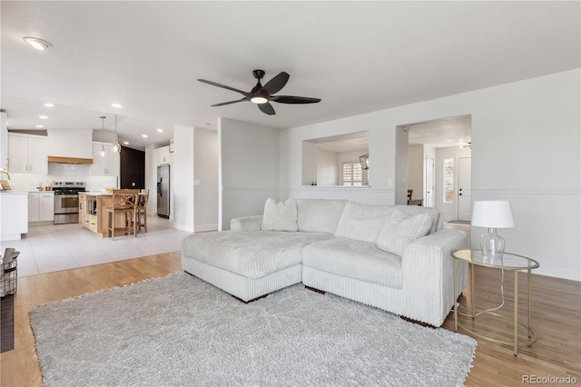 living room with a ceiling fan, light wood-style floors, recessed lighting, and baseboards