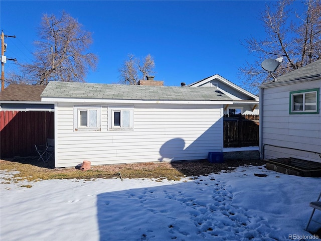 snow covered rear of property with a chimney and fence