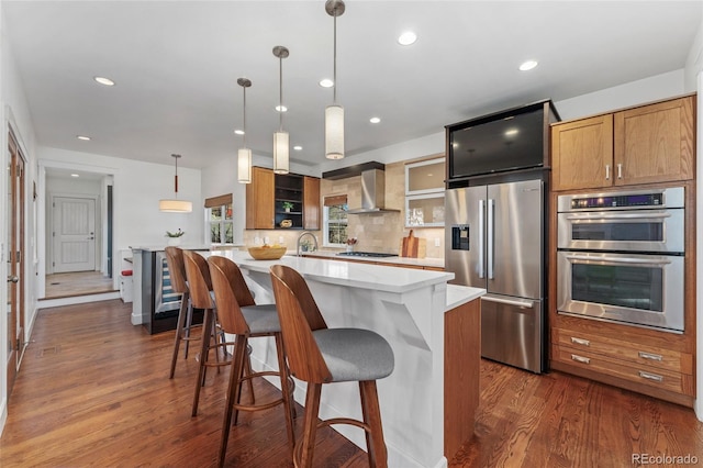 kitchen featuring a kitchen island, a kitchen bar, hanging light fixtures, stainless steel appliances, and wall chimney range hood