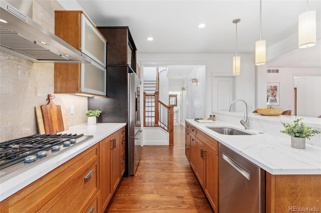 kitchen featuring sink, hanging light fixtures, appliances with stainless steel finishes, light stone countertops, and wall chimney range hood