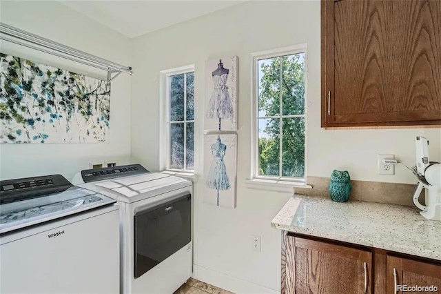 clothes washing area featuring cabinets, a healthy amount of sunlight, and washer and dryer