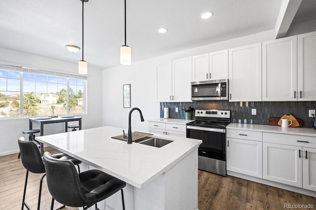 kitchen featuring sink, white cabinets, hanging light fixtures, a kitchen island with sink, and appliances with stainless steel finishes