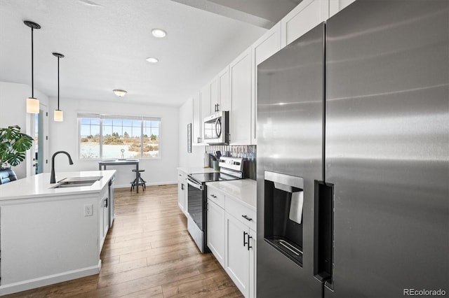 kitchen with decorative light fixtures, a center island with sink, white cabinets, appliances with stainless steel finishes, and sink