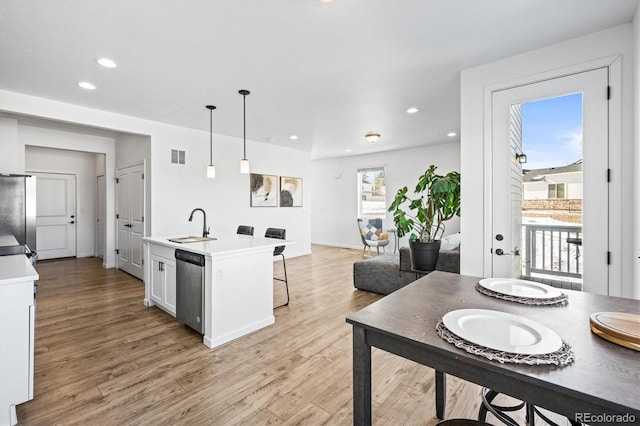 kitchen featuring stainless steel appliances, white cabinets, light hardwood / wood-style flooring, hanging light fixtures, and a kitchen island with sink