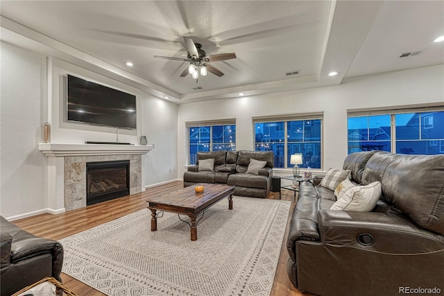 living room with a raised ceiling, visible vents, a tiled fireplace, and wood finished floors