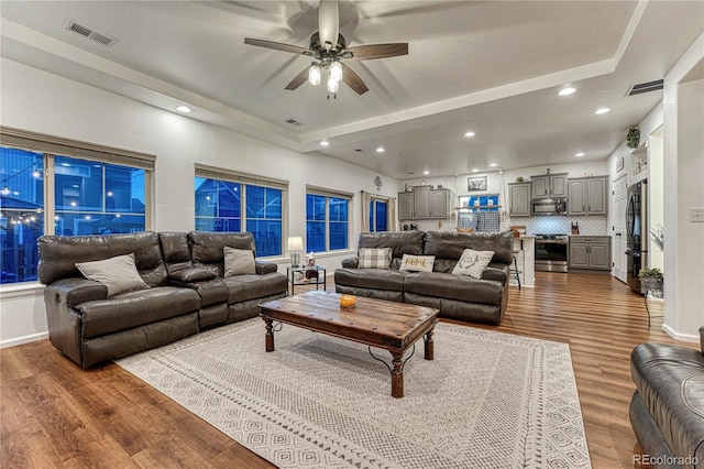 living area with recessed lighting, a raised ceiling, visible vents, and wood finished floors