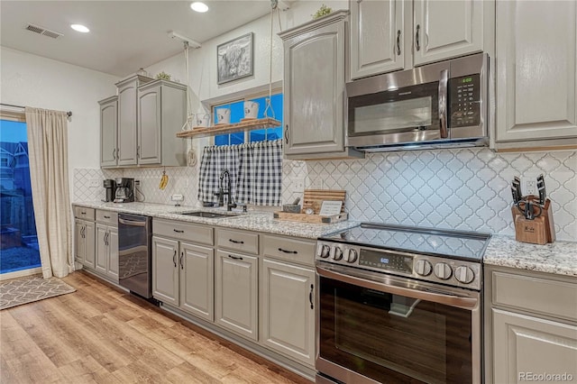 kitchen featuring light stone counters, a sink, visible vents, light wood-style floors, and appliances with stainless steel finishes