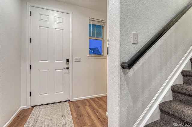 entrance foyer with baseboards, stairway, wood finished floors, and a textured wall