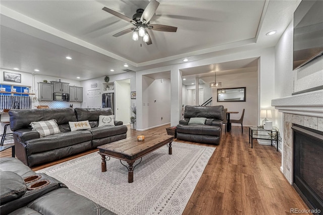 living room featuring recessed lighting, a tray ceiling, wood finished floors, and a glass covered fireplace