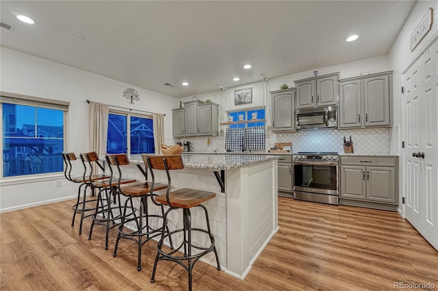 kitchen featuring light wood-style flooring, a kitchen breakfast bar, stainless steel appliances, and gray cabinetry