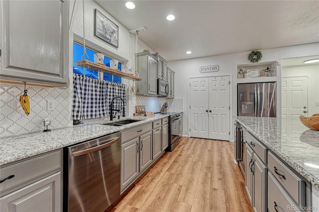 kitchen featuring light wood-style flooring, gray cabinetry, stainless steel appliances, a sink, and decorative backsplash