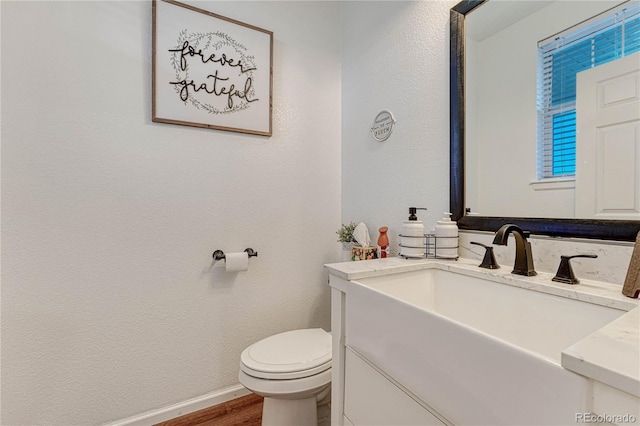 half bath with baseboards, a textured wall, toilet, wood finished floors, and vanity