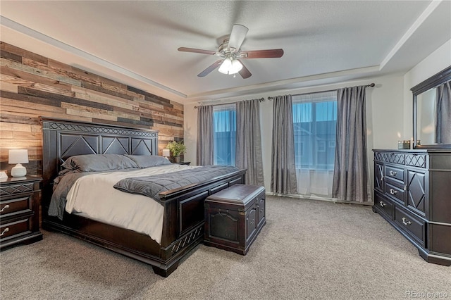 bedroom featuring light carpet, wooden walls, a tray ceiling, and a ceiling fan