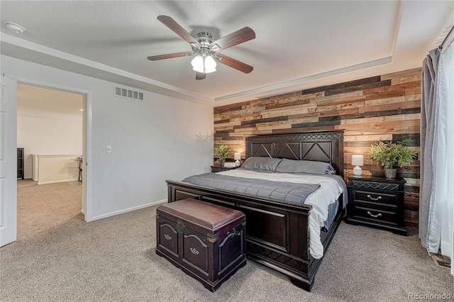 bedroom with light colored carpet, visible vents, a ceiling fan, wooden walls, and baseboards