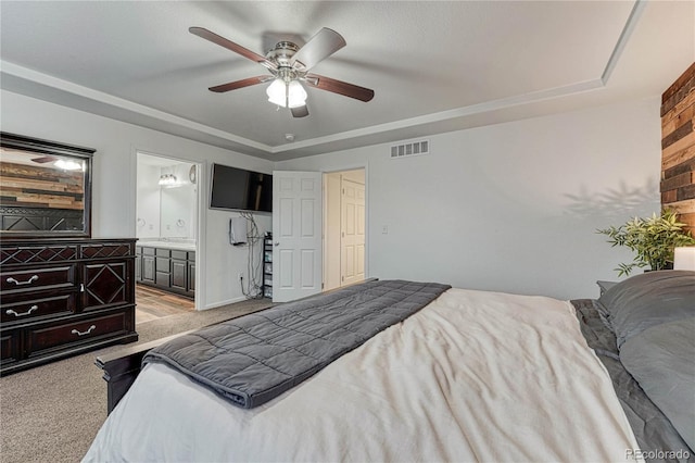 bedroom featuring light carpet, visible vents, a raised ceiling, ceiling fan, and ensuite bath