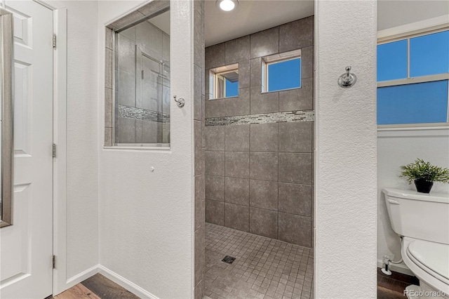 full bathroom featuring a textured wall, toilet, wood finished floors, baseboards, and a walk in shower