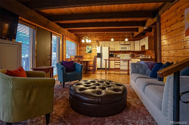 living room featuring rail lighting, an inviting chandelier, beamed ceiling, light hardwood / wood-style floors, and wooden walls