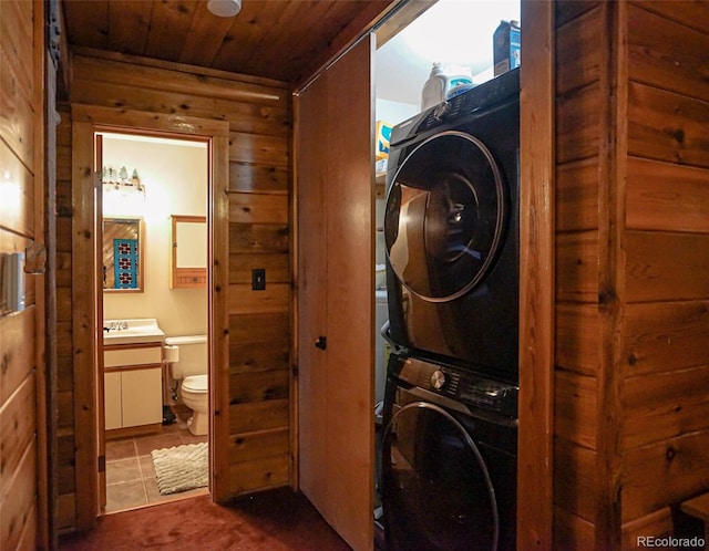 washroom featuring wooden ceiling, dark tile patterned flooring, stacked washer / drying machine, and wood walls