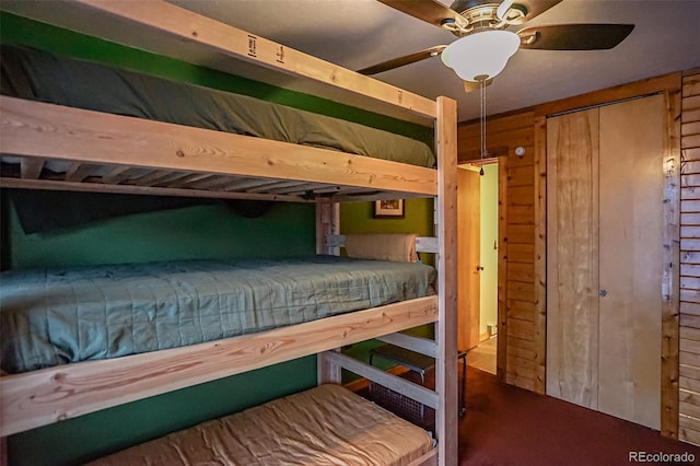 carpeted bedroom featuring a closet, ceiling fan, and wood walls