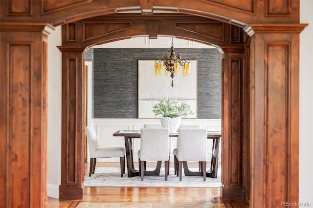 dining room featuring decorative columns, wood finished floors, a decorative wall, a wainscoted wall, and a notable chandelier