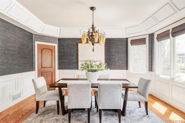 dining space with visible vents, a chandelier, light wood finished floors, and a decorative wall