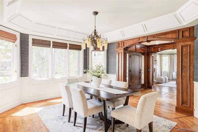 dining space with a notable chandelier, wainscoting, light wood-style flooring, and a decorative wall