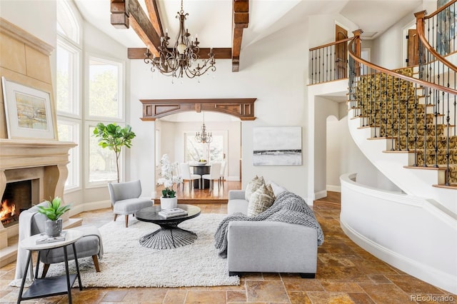 living area with stairway, baseboards, an inviting chandelier, a high ceiling, and stone tile floors