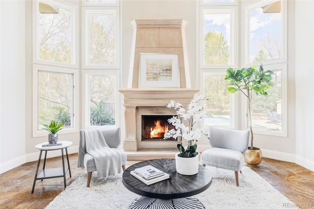 living area featuring stone tile flooring, baseboards, and a warm lit fireplace