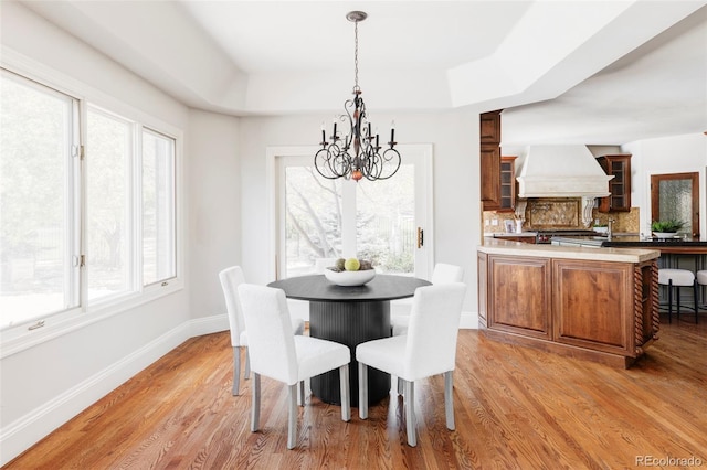 dining room with a notable chandelier, a wealth of natural light, light wood-style flooring, and a raised ceiling