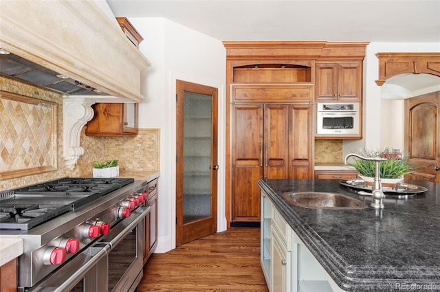 kitchen with decorative backsplash, wood finished floors, custom exhaust hood, wall oven, and double oven range