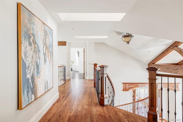 corridor featuring baseboards, wood finished floors, vaulted ceiling with skylight, and an upstairs landing