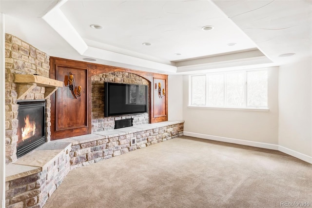 unfurnished living room with a tray ceiling, baseboards, carpet, and a fireplace