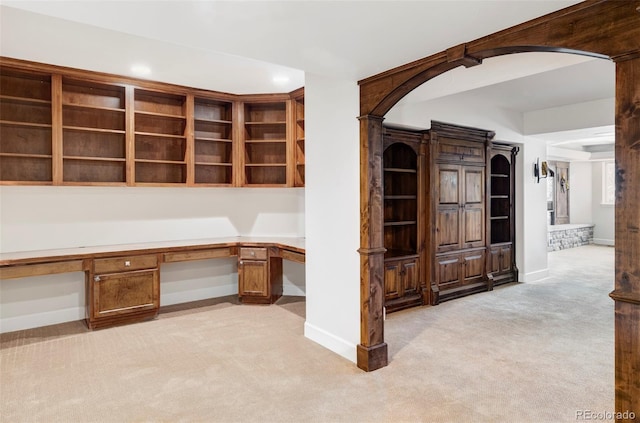 unfurnished office with light carpet, built in study area, baseboards, recessed lighting, and arched walkways