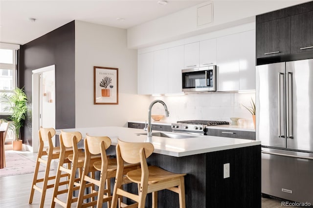 kitchen featuring tasteful backsplash, a kitchen bar, a kitchen island with sink, light hardwood / wood-style floors, and stainless steel appliances