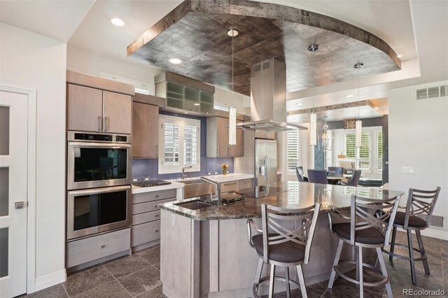 kitchen featuring a kitchen breakfast bar, appliances with stainless steel finishes, island range hood, sink, and dark stone counters