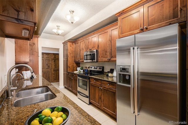 kitchen featuring a sink, dark stone countertops, a textured ceiling, stainless steel appliances, and light tile patterned floors