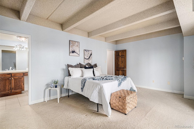 bedroom with beamed ceiling, light colored carpet, ensuite bathroom, and baseboards