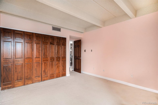 unfurnished bedroom with visible vents, baseboards, beamed ceiling, light colored carpet, and a closet