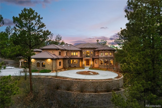 662 Yankakee Dr, Castle Rock, CO 80108 - back of property at dusk with stone siding, a tiled roof, a balcony, and curved driveway