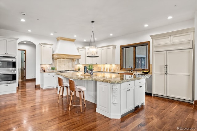 662 Yankakee Dr, Castle Rock, CO 80108 - kitchen featuring an island with sink, tasteful backsplash, stainless steel appliances, custom range hood, and arched walkways