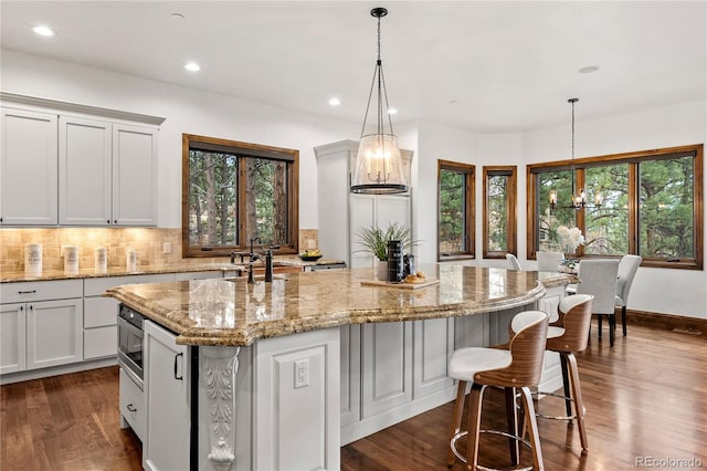 662 Yankakee Dr, Castle Rock, CO 80108 - kitchen with decorative backsplash, a chandelier, a center island with sink, dark wood-type flooring, and light stone counters