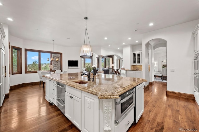 662 Yankakee Dr, Castle Rock, CO 80108 - kitchen featuring a warming drawer, dark wood-type flooring, a center island with sink, a sink, and arched walkways