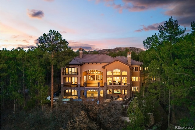 662 Yankakee Dr, Castle Rock, CO 80108 - back of property at dusk featuring a tile roof, stone siding, a chimney, stucco siding, and a balcony