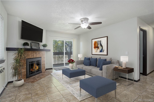 living area featuring a textured ceiling, ceiling fan, light tile patterned floors, a fireplace, and baseboards