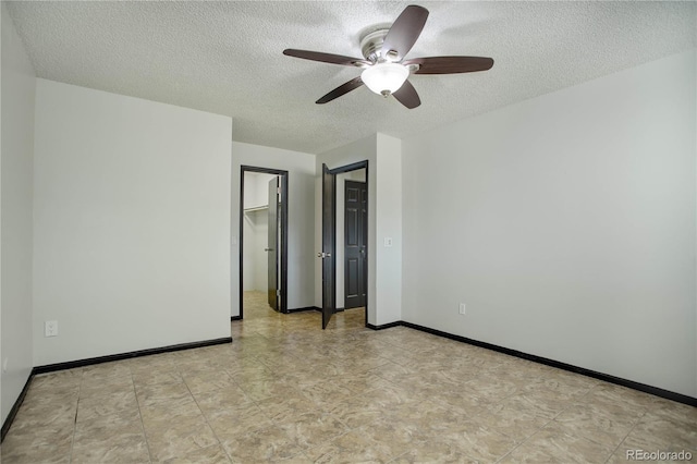 unfurnished bedroom with a ceiling fan, a walk in closet, a textured ceiling, and baseboards