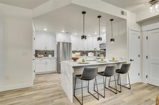 1308 Snowberry Ln Unit 303, Louisville, CO 80027 - kitchen featuring appliances with stainless steel finishes, a kitchen breakfast bar, backsplash, light wood-style floors, and white cabinets