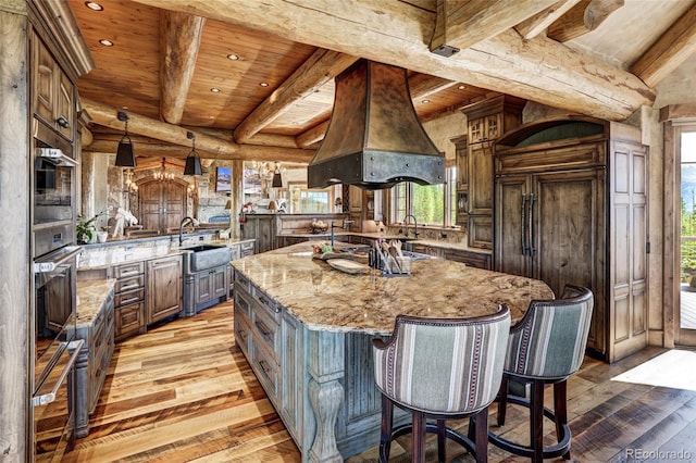 kitchen featuring a spacious island, light stone counters, hanging light fixtures, beam ceiling, and range hood