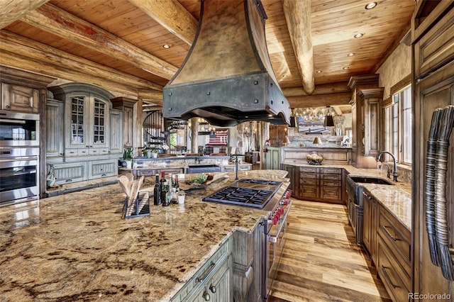 kitchen featuring stainless steel appliances, light stone counters, custom range hood, log walls, and wooden ceiling