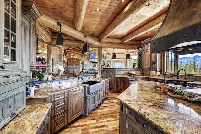 kitchen featuring light wood finished floors, glass insert cabinets, beamed ceiling, pendant lighting, and a sink